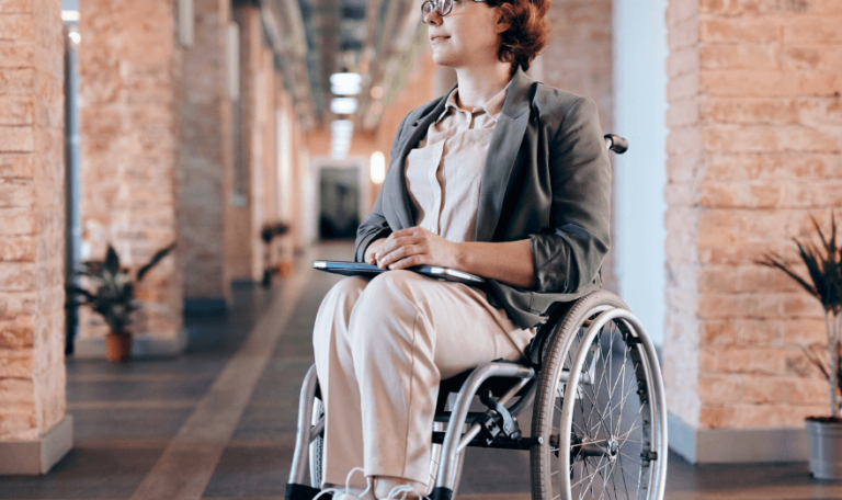 Business woman wearing glasses using a wheelchair. She is carrying an iPad, and admiring the architecture of the building.